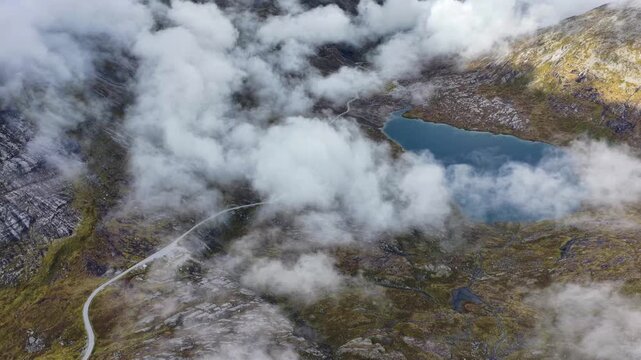 Aerial view of the winding Trollstigen road and Alnesvannet lake surrounded by dramatic mountains and low clouds in Andalsnes, More og Romsdal, Norway.
