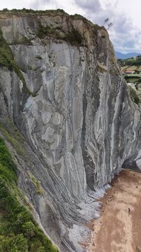 Stunning vertical aerial drone footage panning from a close-up of the dramatic, towering vertical flysch rock strata at Itzurun Beach towards the vast Atlantic Ocean &ndash; 2026
