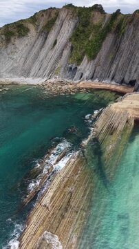 Stunning vertical aerial drone footage flying forward and approaching the dramatic towering vertical flysch rock strata and cliffs of Itzurun Beach in Zumaia, Spain &ndash; 2026