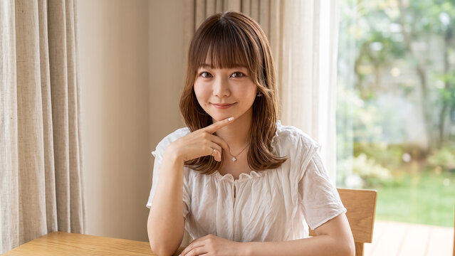 Young smiling Japanese woman resting chin on hand at home with natural light and bright interior, friendly portrait of a smiling female