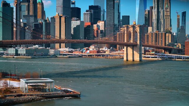Brooklyn Bridge and Lower Manhattan skyline from Dumbo. Snow patches dot the waterfront as boats cross the river beneath the historic suspension bridge.