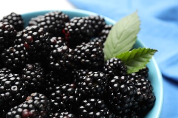 Many fresh blackberries and green leaves in bowl on light table, closeup © New Africa