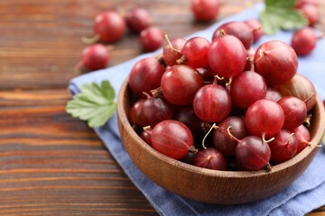 Fresh red gooseberries, green leaves and bowl on wooden table, closeup. Space for text © New Africa