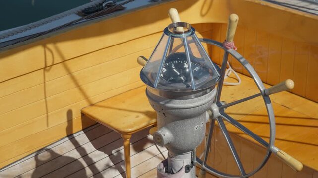 A vintage marine compass and ship helm stand on a classic wooden yacht deck. Traditional nautical instruments guide maritime navigation. Steering gear symbolizes leadership and direction.