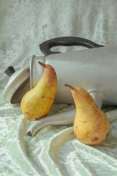 Pears beside a silver kettle on a soft fabric surface