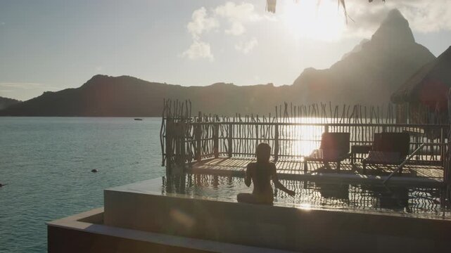 Luxury travel vacation resort. High end hotel pool. woman tourist relaxing watching sunset on private balcony terrace of overwater bungalow suite in Bora Bora, Tahiti, French Polynesia