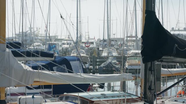Sailboats and motorboats dock together in a crowded marina harbor. Dense masts and rigging create a detailed nautical background. The busy seaport offers safe boat storage and yacht maintenance.