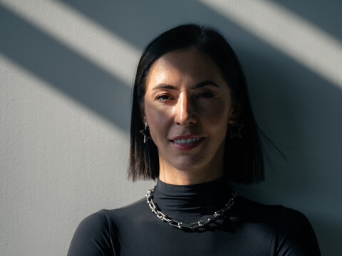 Woman Poses in Front of a Wall With Light and Shadow Patterns