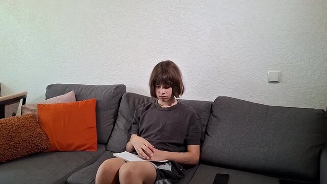 13 year old boy reading a book on a couch in a living room during afternoon