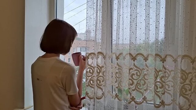 13 year old boy looks out the window and observes the rain falling outside