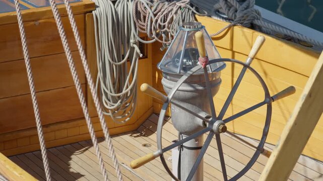 Sailboat steering wheel with compass stands in wooden cockpit. Nautical helm guides maritime navigation and travel. Vessel binnacle symbolizes leadership, strategic direction, and control.