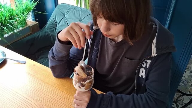 13 year old boy enjoys dessert at cafe while sitting at a wooden table in a cozy setting