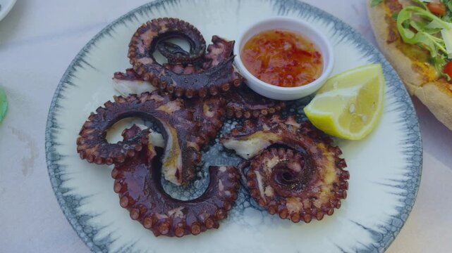 Grilled Octopus Tentacles Served With Sweet Chili Sauce Dip Bowl And Fresh Lemon. Delicious Seafood Appetizer Delicacy