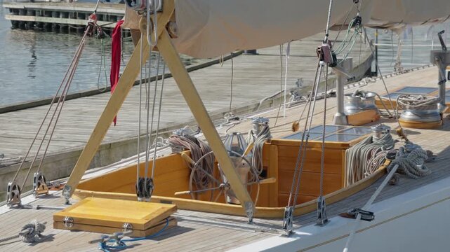 Classic wooden sailboat moors at harbor dock with teak deck. Detailed rigging showcases traditional yacht craftsmanship. Vintage boat offers luxury sailing heritage and maritime maintenance.