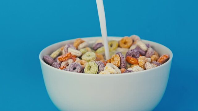 Fresh milk poured over a bowl of colorful cereal against a vibrant blue background