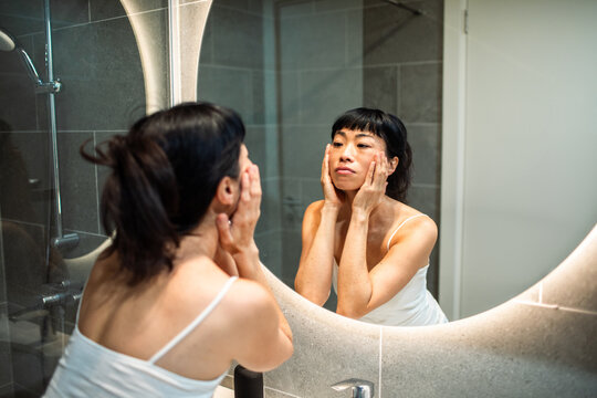 Woman applying skincare in bathroom mirror