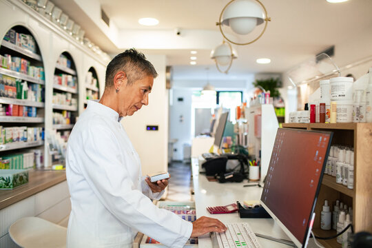 Pharmacist checking medication at computer in modern pharmacy