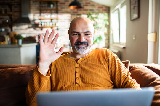 Smiling man waving on laptop video call at home
