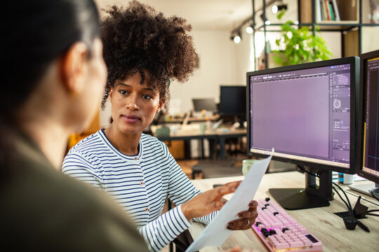 Coworkers discussing design project at computer in modern office