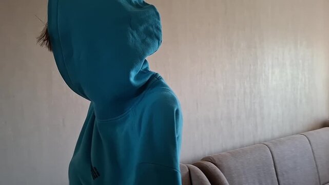 13 year old boy folds a large blue cloth in a room on a bright afternoon