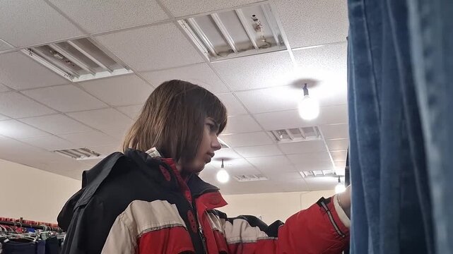 13 year old boy shops in clothing store while browsing racks of clothes in the changing room area