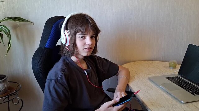 13 year old boy sits at a table listening to music while using a smartphone