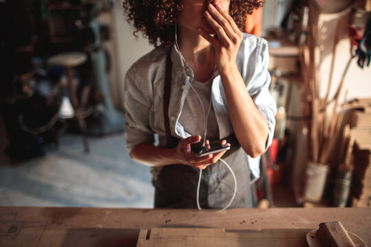 Thoughtful artisan using smartphone in woodworking studio
