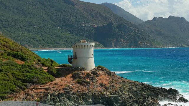 Albo Genoese tower drone approach Cap Corse Corsica 70mm telephoto black beach, turquoise sea waves, dramatic mountain background, dark pebble coast, cinematic drone 4k footage