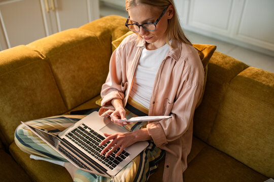 Young woman paying bills on laptop on the sofa at home