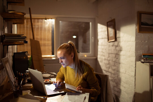 Focused young woman studying on laptop in home office at night