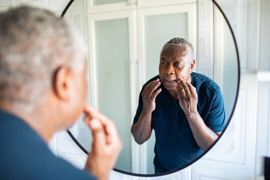 Senior man checking face in bathroom mirror