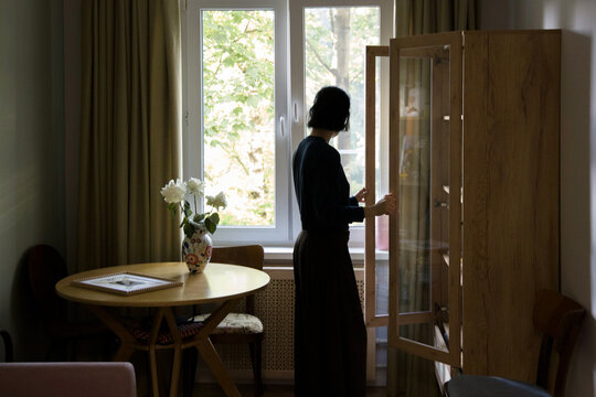 Woman stands by cabinet in a room with a table and flowers