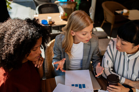Three businesswomen discussing data at outdoor cafe