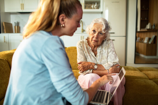 Caregiver helping senior woman with laptop at home