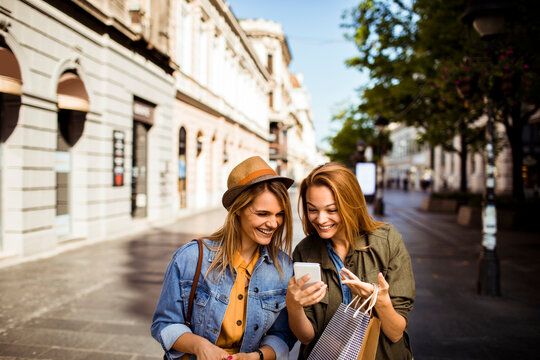 Two friends shopping and looking at smartphone on city street