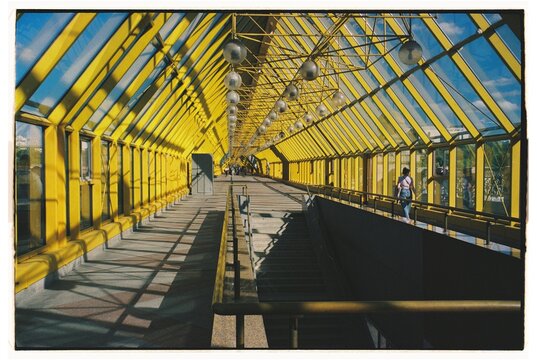 Sunlight streams through a glass walkway with yellow frames
