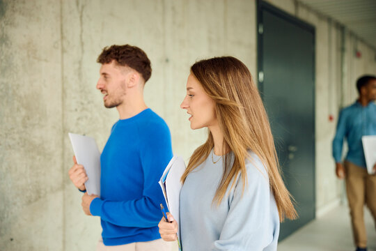 Two People Walking in a Hallway With Papers in Their Hands