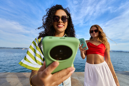 Women on vacation recording content with smartphones by the sea