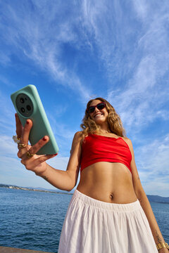 Young woman taking selfie with smartphone by the ocean