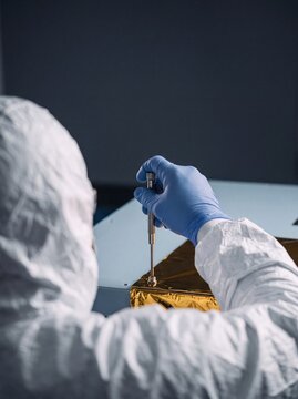 Engineer in a protective cleanroom suit and gloves assembling aerospace satellite components with a precision screwdriver
