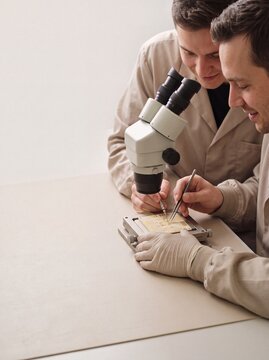 Two male engineers assembling microelectronics under a stereo microscope in a modern laboratory