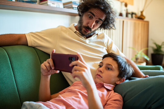 Father and son watching smartphone on living room couch