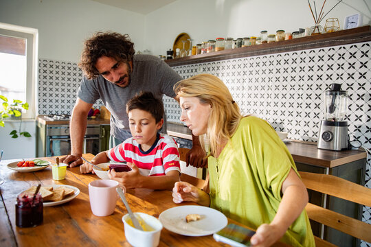 Parents and son using smartphone during breakfast at home kitchen