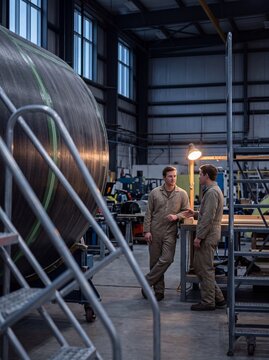 Two aerospace engineers talking next to a large composite carbon fiber component in an industrial manufacturing hangar