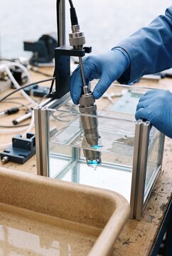 Scientist in protective gloves calibrating an optical sensor probe submerged in a water tank in a laboratory