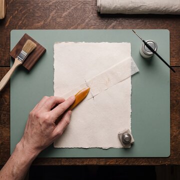 Artisan conservator carefully mending a tear on vintage handmade paper using repair tissue and a wooden burnisher tool