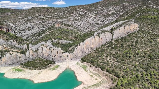 Wide panoramic view moving backwards from the iconic twin rock formations and historical ruins of Castell de Finestres over the stunning blue waters of the surrounding lake &ndash; 2026