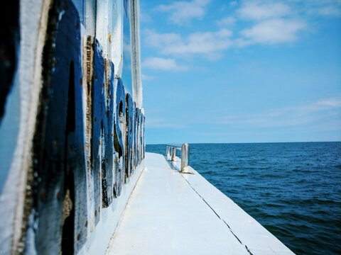 Side view of boat deck with blue painted metal railing overlooking deep blue ocean horizon under clear sky