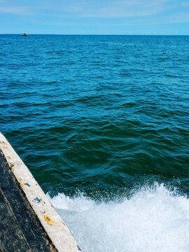 Deep blue ocean waves with white sea foam splashing from moving boat in bright natural daylight