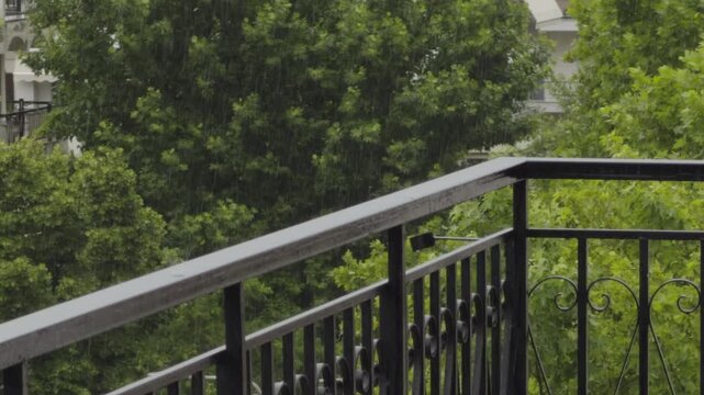 Rain Drops Falling On Balcony Metal Railing With Green Trees. Rainy Weather